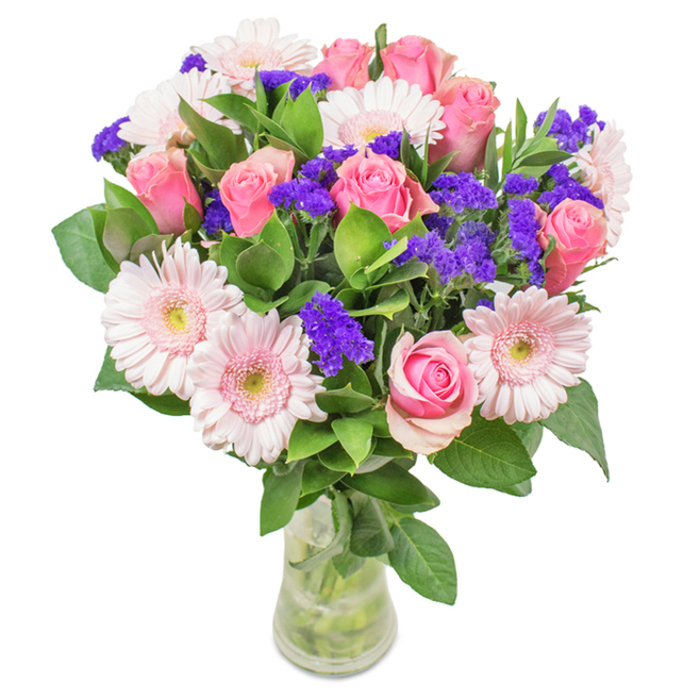 An elegant and vibrant floral bouquet overflows from a crystal-clear vase, capturing the classic and refined aesthetic beloved throughout Totteridge. The centrepiece reveals seven to nine lush pink roses, their petals in varying states from tightly closed to gently opening, displaying the iconic spiral formation. These roses are perfectly harmonized with five to seven pale pink gerbera daisies-large, round blooms with delicate, radiating petals and lighter, almost white centres. Bright purple statice peeks between the larger flowers, offering vivid contrast, fine texture, and depth. Around the design, abundant green foliage fans out, adding freshness and a touch of the natural abundance seen in Totteridge's leafy avenues and parks. Clear water fills the glass vase, nourishing the stems and adding a final note of purity. The bouquet's composition makes it ideal as a birthday gift, an anniversary sentiment, a tribute for Mother's Day, or a graceful addition to home or office-delivering a flourish of joy, celebration, and local warmth from your Totteridge florist.